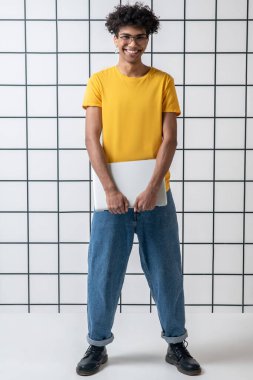 Gözlüklü Afro-Amerikan genç adam dizüstü bilgisayar tutuyor.