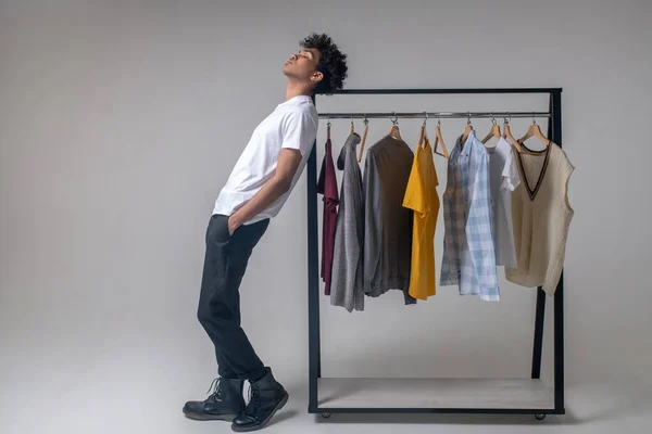 Lockig ung kille står nära hängarna med kläder — Stockfoto