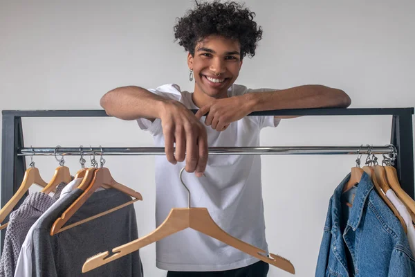 Afrikanischer junger Mann in der Nähe von Kleiderbügeln mit lächelnden Kleidern — Stockfoto