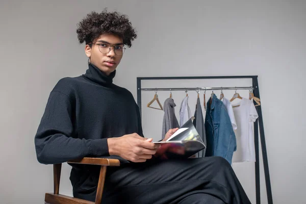 Afro-américain jeune homme portant des vêtements noirs assis dans un showroom — Photo
