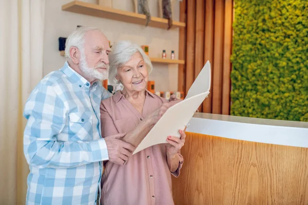 Gray-haired couple standing near reception in a spa center — Stock Photo, Image