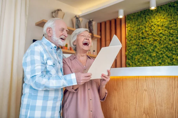 Grauhaariges Paar steht in der Nähe der Rezeption in einem Wellness-Center und lacht — Stockfoto