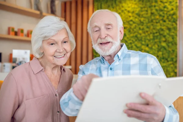 Gray-haired couple looking trhough the price list in spa center and looking excited — Stock Photo, Image