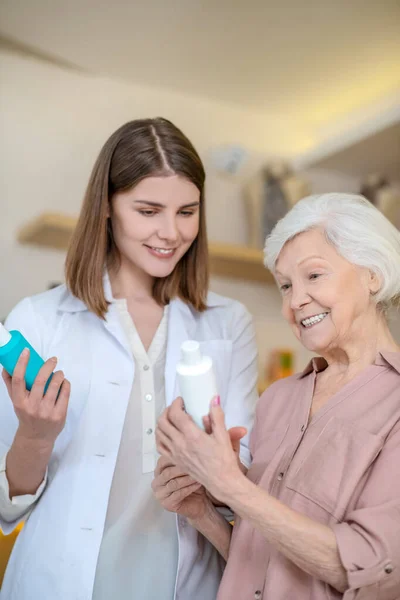 Joven cosmetóloga morena demostrando nuevos productos cosméticos a una clienta — Foto de Stock