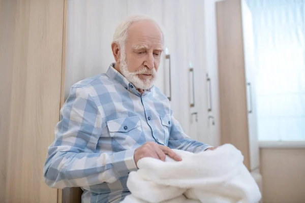 Gray-haired mature man in a changing room in spa center with towels in hands — Stock Photo, Image