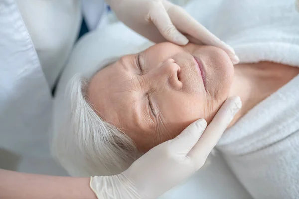 Grijs-harige volwassen vrouw met een gezicht massage en op zoek ontspannen — Stockfoto