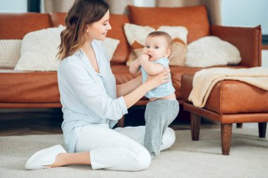Woman sitting on floor supporting child with hands