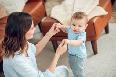 Smiling baby standing holding moms hands