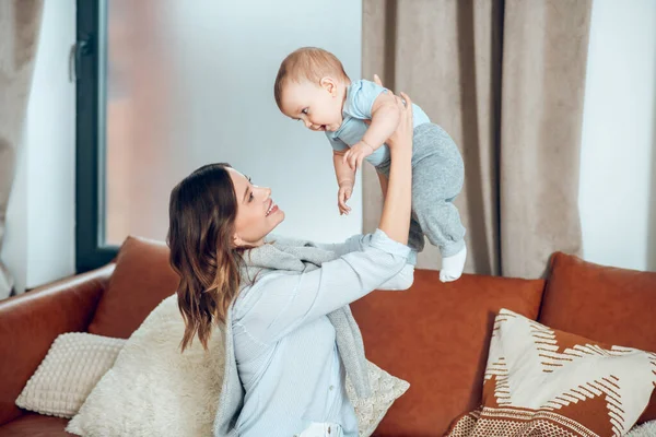 Smiling young mother with baby in raised arms — Stockfoto