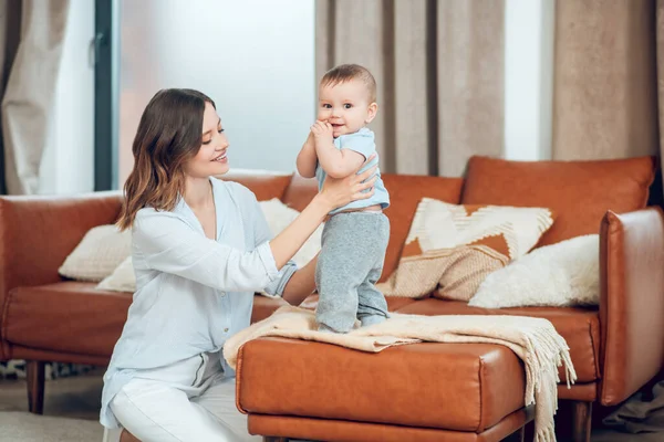 Young woman supporting child standing on sofa — Stockfoto