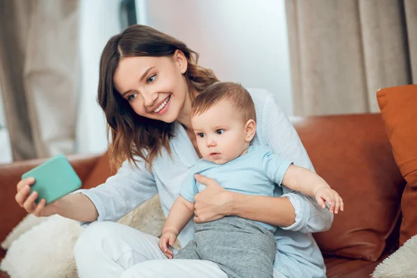 Mom with child looking at smartphone in outstretched hand — Stock Fotó