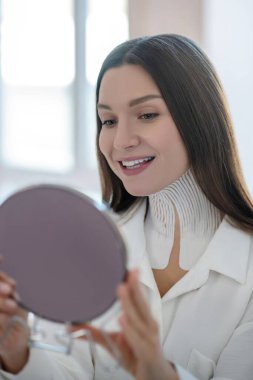 Cute young woman with tapes on her neck looking in the mirror