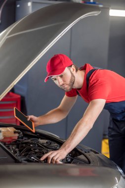 Auto mechanic with tablet examining car under hood