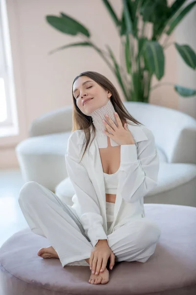 Young woman in white sitting on a round chair with tapes on her neck — Fotografia de Stock