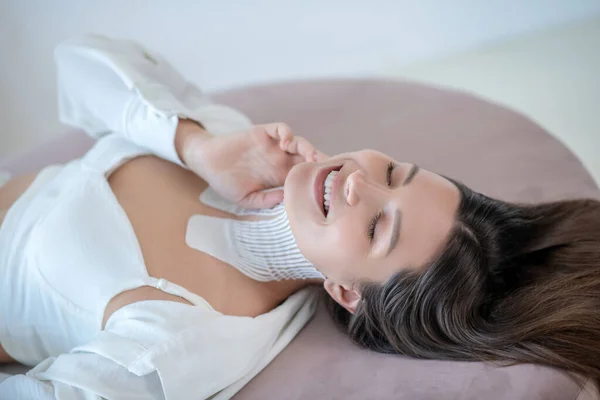 Young woman in white lying with tapes on her neck and looking relaxed — Fotografia de Stock