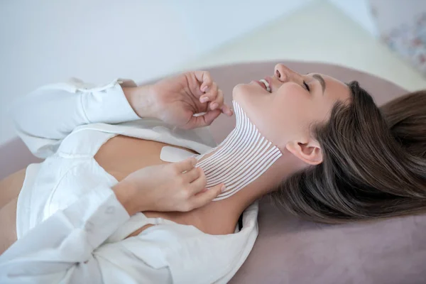 Young woman in white lying with tapes on her neck and looking peaceful — kuvapankkivalokuva