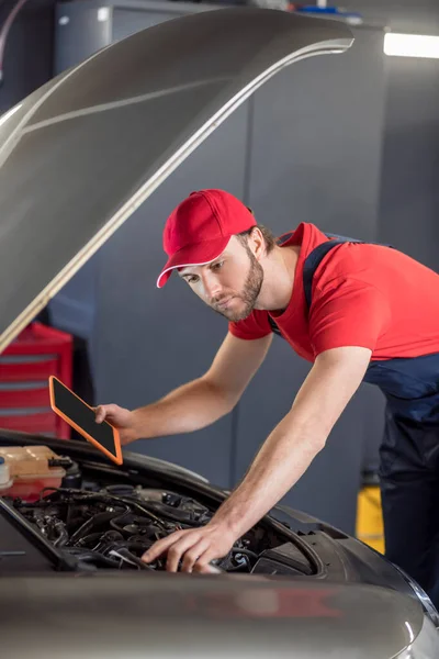 Auto mechanic with tablet examining car under hood — Stock Photo, Image