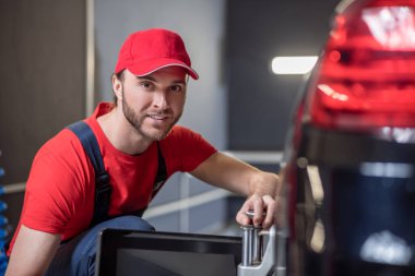 Happy man crouched working near car wheel