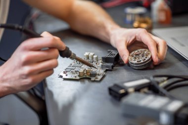 Male hands touching microcircuit with soldering iron