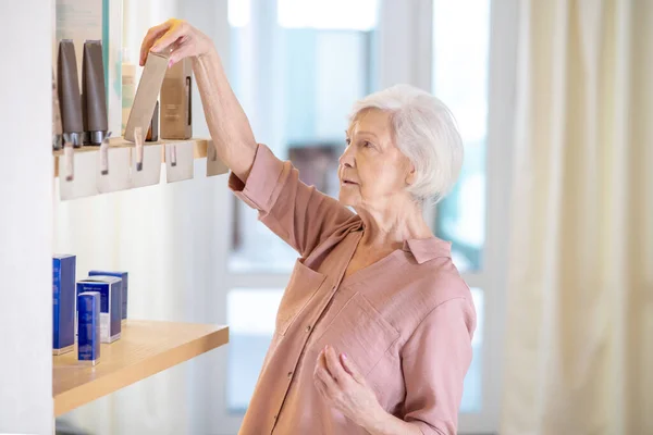 Mujer madura de pelo corto que elige perfumes en una boutique — Foto de Stock