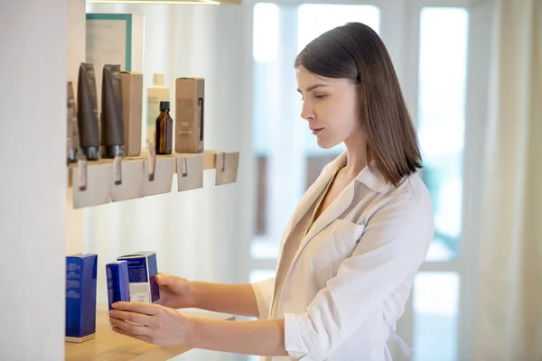 Joven asistente de tienda de cabello oscuro examinando los nuevos cosméticos en una tienda — Foto de Stock