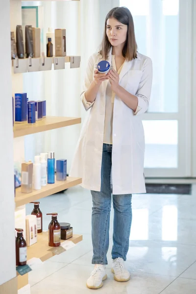 Esmer genç tezgahtar bir dükkanda yeni kozmetik ürünlerini inceliyor. — Stok fotoğraf