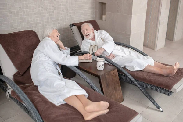 Mature couple in white robes lying on a chaise lounges in a spa center — Stock Photo, Image