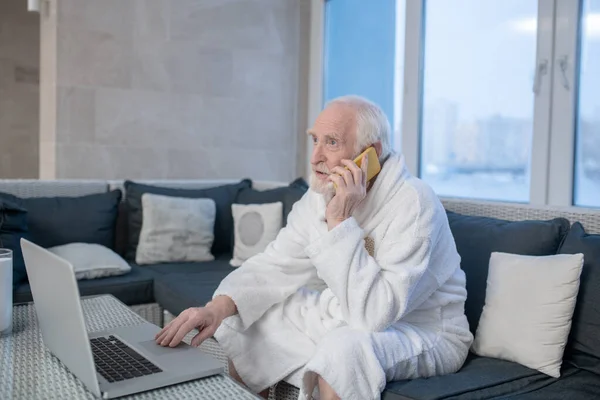Homem de cabelos grisalhos em um manto branco com um laptop — Fotografia de Stock