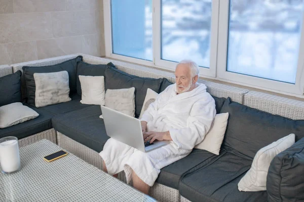 Hombre de pelo gris con una túnica blanca con un portátil — Foto de Stock