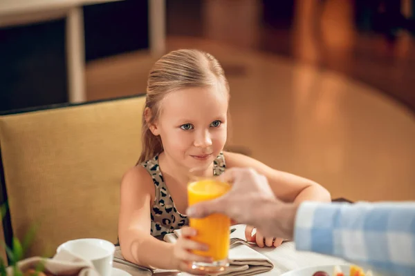 Мила дівчина сидить за столом і п'є апельсиновий сік — стокове фото