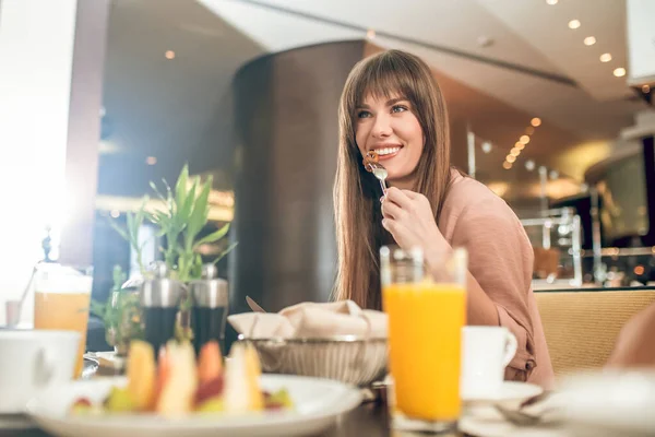 Mujer joven de pelo largo desayunando y buscando contenta — Foto de Stock