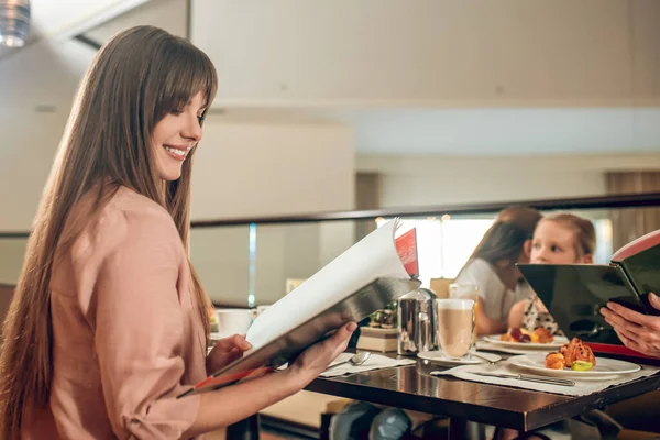 Young woman holding a menu and choosing what to order — Stock Photo, Image