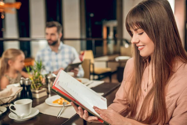 Ung kvinna som håller en meny och välja vad du vill beställa — Stockfoto