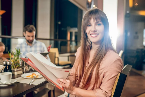 Young woman holding a menu and choosing what to order — Stock Photo, Image