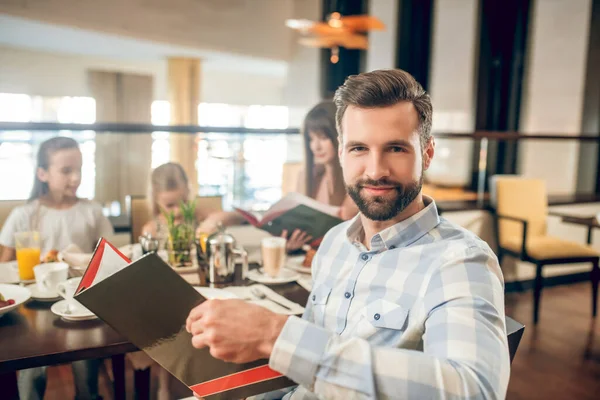 Junger Mann hält ein Menü in der Hand und wählt, was bestellt werden soll — Stockfoto