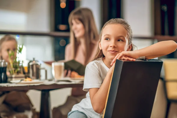 Dulce chica sentada en la mesa en el restaurante con la familia — Foto de Stock