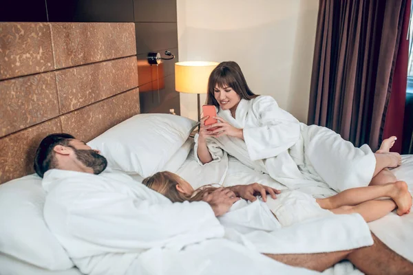 Gezin in witte gewaden liggend in bed en op zoek ontspannen — Stockfoto