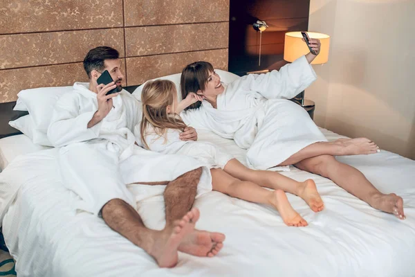 Beyaz elbiseli bir aile yatakta uzanıyor ve rahatlamış görünüyor. — Stok fotoğraf