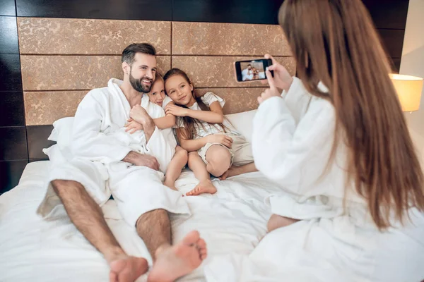 Семья в белых халатах лежит в постели и делает селфи — стоковое фото