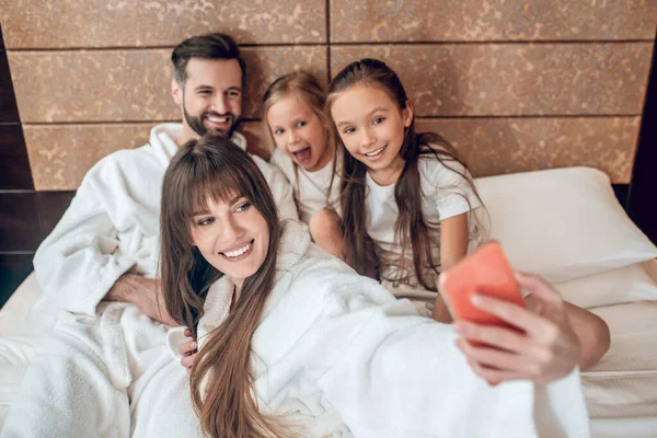 Семья в белых халатах лежит в постели и делает селфи — стоковое фото