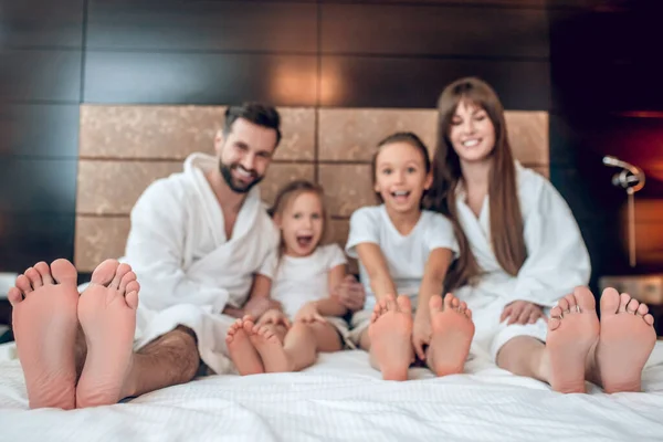 Семья в белых халатах лежит в постели и выглядит счастливой — стоковое фото