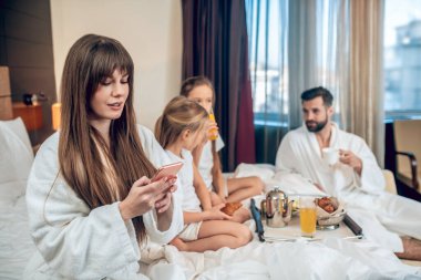 Uzun saçlı kadın, ailesi kahvaltı ederken telefonla konuşuyor.