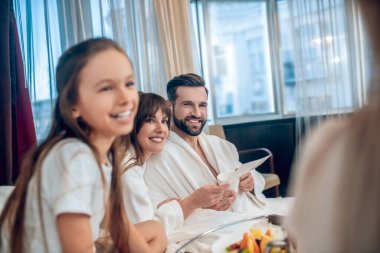 Ebeveynler ve çocuklar kahvaltı yapıyor ve halinden memnun görünüyorlar.