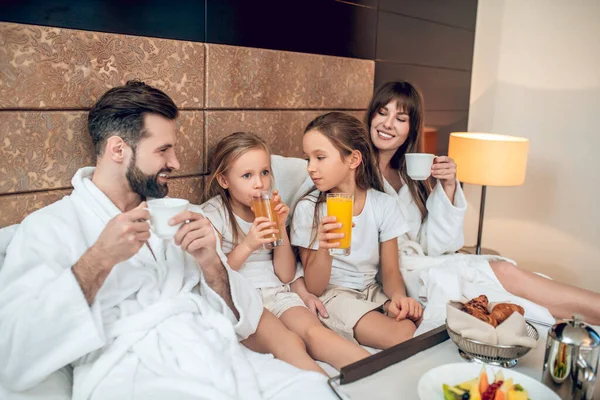 Beyaz cüppeli bir aile yatakta uzanıyor ve kahvaltı yapıyor. — Stok fotoğraf