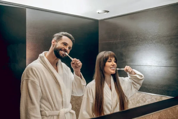 Pareja joven en batas de baño cepillándose los dientes juntos — Foto de Stock