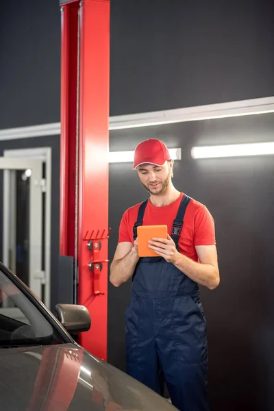 Auto monteur op zoek naar tablet in de buurt van auto — Stockfoto