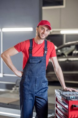 Tulumlu çekici bir adam araba tamirhanesinde duruyor.