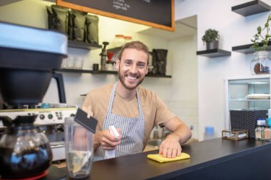 Barın arkasında peçeteli ve dezenfektanlı mutlu bir adam.
