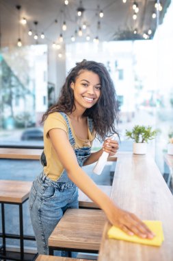 Kafedeki masaları silen neşeli bir kadın.