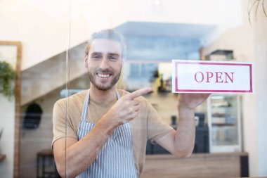 Kafenin girişindeki tabelayı gösteren adam.